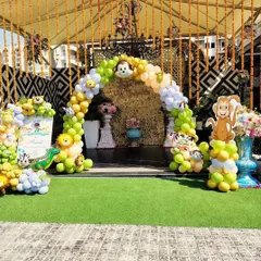 An outdoor jungle theme entrance arch for a party. The setup includes a lush green turf floor, a balloon arch with monkey characters, and hanging floral decorations.
