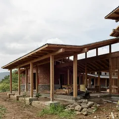 The farmhouse in Kamshet is defined by its long, covered verandas supported by a timber frame structure. These spaces provide shelter from the sun and rain while maintaining a constant connection to the surrounding landscape.