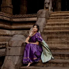 A wide shot capturing a vintage, poetic mood against the backdrop of ancient temple stairs. Dressed in a purple saree, this image tells a story of history, grace, and quiet contemplation.