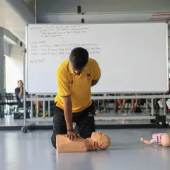 A coach's responsibility goes beyond the field. This image from our 'Restart a Heart' workshop shows a participant practicing essential CPR chest compressions on a manikin, a skill that can save a life.