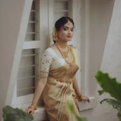 An elegant portrait of a Kerala bride in a classic cream and gold saree, posed near a window for soft, natural light.