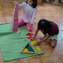Here, two children collaborate naturally. One works with the Pink Tower, learning about size and dimension, while the other explores geometric shapes. This demonstrates how children learn from each other in our mixed-age classrooms.