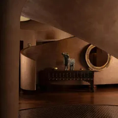 The interior of the House of Masaba, where the earthy, terracotta-toned lime plaster creates a warm, cave-like feel. Traditional artifacts are placed in dialogue with the modern, sculptural architecture.