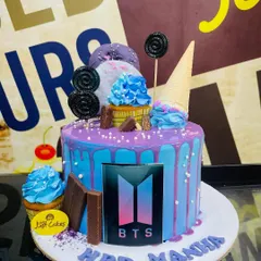 A fan's dream come true, this custom cake is designed for a BTS lover's birthday. The cake features a blue and purple drip design and is decorated with lollipops, cupcakes, and an edible print of the BTS logo right on the front.