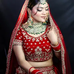 A beautiful side profile of a bride in a classic red lehenga. The focus here is on the harmony between the rich green jewelry and the warm tones of the makeup, demonstrating an understanding of color theory in bridal styling.