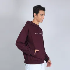 A side-profile shot of the same maroon hoodie, showing the fit and how the model interacts with the garment by placing a hand in the pocket.