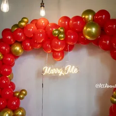 A close-up of the 'Marry Me' neon sign nestled within the vibrant red and gold balloons, adding a modern and heartfelt touch.