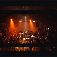 A wide shot of a packed warehouse-style venue. The industrial setting and focused lighting create the perfect atmosphere for a night of deep, underground techno.