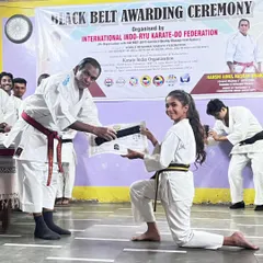 The official Black Belt Awarding Ceremony. Here, a senior master presents Lekissha with her belt and certificate, a formal recognition of her achievement in front of her peers.