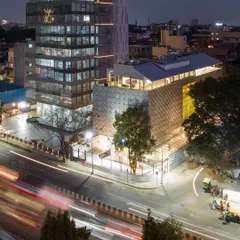 An aerial view of the MAP museum at night, showing its relationship with the surrounding urban environment of Bangalore. The building is designed to be a beacon in the city's museum quarter, with its illuminated facade and rooftop restaurant contributing to the public life of the street.