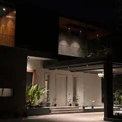 The entrance of "The One" residence is dramatic and welcoming after dark. Strategic lighting accentuates the large canopy, the texture of the walls, and the lush plants, guiding visitors toward the front door with a sense of quiet grandeur.