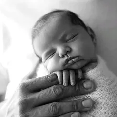 The comfort of a parent's touch. This image showcases the gentle and secure way we handle newborns, capturing a moment of pure peace and trust.