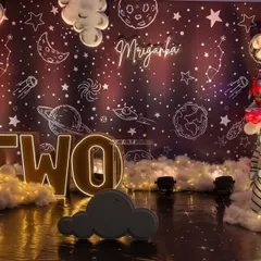 A spectacular 'Two The Moon' space-themed 2nd birthday party. The backdrop features a galaxy print, light-up letters, a moon prop, and fluffy clouds, creating a universe of fun for the little one.