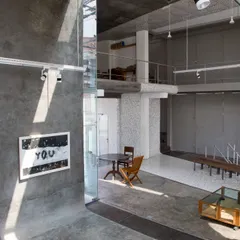 The interior of the Artrovert studio, featuring raw concrete surfaces, double-height volumes, and a mezzanine study. The space is designed to be rugged, flexible, and filled with natural light.