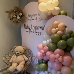 A sweet and modern baby shower setup with a "Mashup of Love" theme. This features a custom arched backdrop, a soft pastel balloon garland, and a cute teddy bear on a wicker peacock chair.