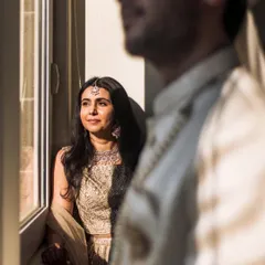 An artistic shot using natural window light. The bride looks out thoughtfully while the groom is softly focused in the foreground, creating a sense of anticipation.