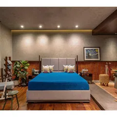 The master bedroom in "Between Two Trees" features a platform bed and a backdrop of textured walls and wood paneling. The design is minimal yet warm, creating a calming environment.