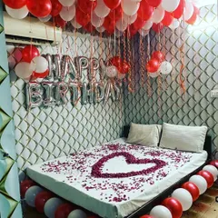 A classic romantic birthday surprise with a bed decorated with a heart made of rose petals, and red and white balloons filling the room.