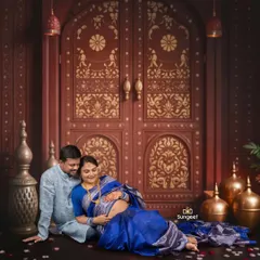 An intimate moment between an expecting couple, captured against a traditional, ornate backdrop. The rich blue sarees and coordinated ethnic wear add a touch of cultural elegance to their maternity photoshoot.