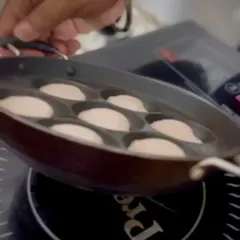 The process of making paniyaram live at an event. A chef carefully lifts the special pan from an induction cooktop, showing how we prepare these South Indian delicacies fresh for guests.