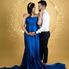 A glamorous couple's portrait. Dressed in a stunning blue satin gown, the mom-to-be shares a loving gaze with her partner, framed by a sparkling golden ring light.