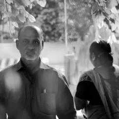 A fleeting moment captured in black and white. This candid street portrait uses natural framing from the leaves to create depth and focuses on the man's direct gaze, telling a story without a single word.