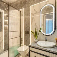 This bathroom features a sophisticated palette of grey marble and fluted textures. The oval LED mirror and vessel sink on the suspended vanity create a modern and elegant focal point.
