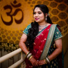 This bride's reception style is both elegant and modern. Her side-swept hair, diamond jewelry, and glowing makeup create a sophisticated look against the backdrop of the 'Om' symbol.