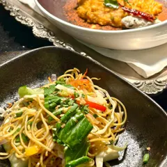 A pairing of our global culinary offerings. In the foreground, a vibrant Asian noodle salad, and in the background, a contemporary take on a South Indian dish, showcasing our ability to plate diverse cuisines with precision and style.