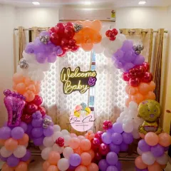 A 'Welcome Baby' ring decoration in pastel shades of purple, orange, and pink. This setup includes a neon sign and cute baby-themed foil balloons.
