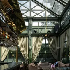 The grand, double-height interior, where a brass-clad bar canopy reflects the light from the glass ceiling. The scale is dramatic, yet the seating arrangements create intimate, comfortable zones.