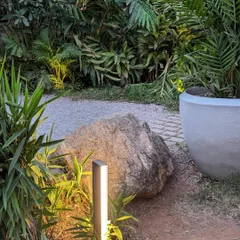 A small, modern light fixture casts a warm glow on the surrounding plants and a large boulder. Even small lights, when placed strategically, can have a major impact on the garden's nighttime atmosphere.