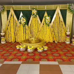 A Haldi ceremony stage featuring a geometric wooden frame, hanging marigold strings, and traditional brass pots, creating a modern yet ethnic look.