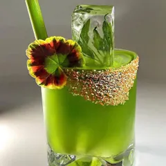 A vibrant green cocktail showcasing my focus on presentation. It features a custom-rimmed glass, a large ice cube with herbs frozen inside, and an edible flower garnish.