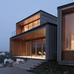 We call these the glowing portals of the Lakehouse in Hyderabad. As dusk settles, the wood-clad volumes frame the landscape, creating a dramatic and serene connection between the home and the distant city lights over the water.
