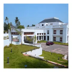 A daytime view of a grand residence in Kerala, showcasing clean architectural lines against soft, rolling lawns. The landscape design incorporates gentle slopes and strategically placed lighting to complement the building's stately presence.