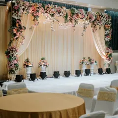 For a classic and elegant reception, I designed this stage with a lush floral arch over soft, draped fabric. Spotlights and elegant floral urns complete the look, creating a timeless space for celebration.
