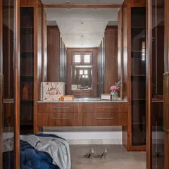 This walk-in closet is a dream of organization. The glass-fronted wardrobes keep things visible but dust-free, while the central vanity and plush ottoman add a touch of luxury. It's a beautiful and functional private space.