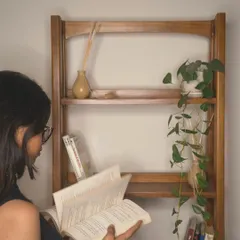 This image captures the experience of using the bookshelf, creating a personal library corner in your home. The solid teak construction ensures it will be a part of your story for years.