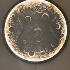 The black-framed moon lamp, glowing warmly. The light creates beautiful shadows in the craters, making it look incredibly realistic.