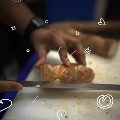 A freshly baked baguette being sliced, revealing its crisp crust and soft interior. This is one of the classic breads you'll learn to make in our artisan baking class.