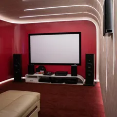 A vibrant and modern media room design. The bold red wall with acoustic tiling, combined with curved LED lighting, creates a dynamic space that's perfect for movies, gaming, and music.