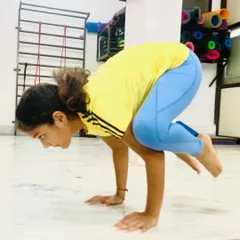 A student practicing Bakasana (Crow Pose), a foundational arm balance that builds wrist strength and core control.