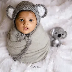 Hello, little koala! This newborn is wrapped in grey and wearing an adorable crocheted koala hat, looking right at the camera.