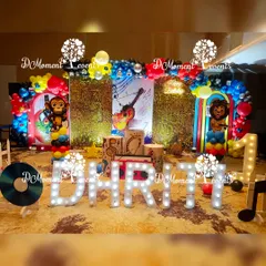 A vibrant and energetic Musical-themed first birthday stage. The decor features a sequin backdrop, musical note cutouts, a large guitar graphic, and fun animal characters playing instruments.