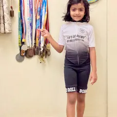 A young skater proudly wearing her academy suit next to her collection of medals. She is born to roll and built to win.