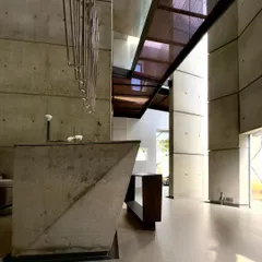The main living area of the 'House of Stories' project, where a custom concrete console and sculptural steel elements interact with the tall, light-filled volume. The design is an exercise in minimalism, allowing the architecture itself to be the primary feature.