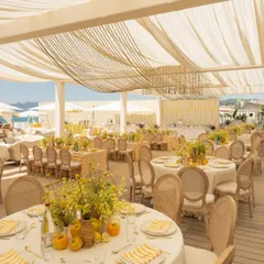 The dining setup for the Cannes Mehendi featured round tables with yellow and white striped linens, rattan chairs, and fresh yellow floral centerpieces, creating a cheerful, summery vibe.