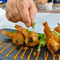 Precision meets passion. Here, our chef adds a delicate microgreen, the final touch to our Panko Crumb Chimichurri Prawns, ensuring every plate is a work of art.