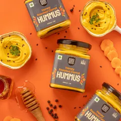 A top down shot of Honey Roasted Carrot Hummus. The styling includes the key ingredients like carrots and honey, which visually tells the story of the product's flavor. The color palette is warm and inviting.